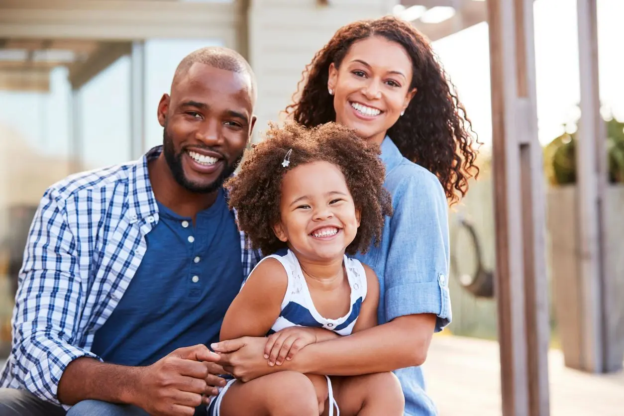 A man and woman with a child in front of a house.